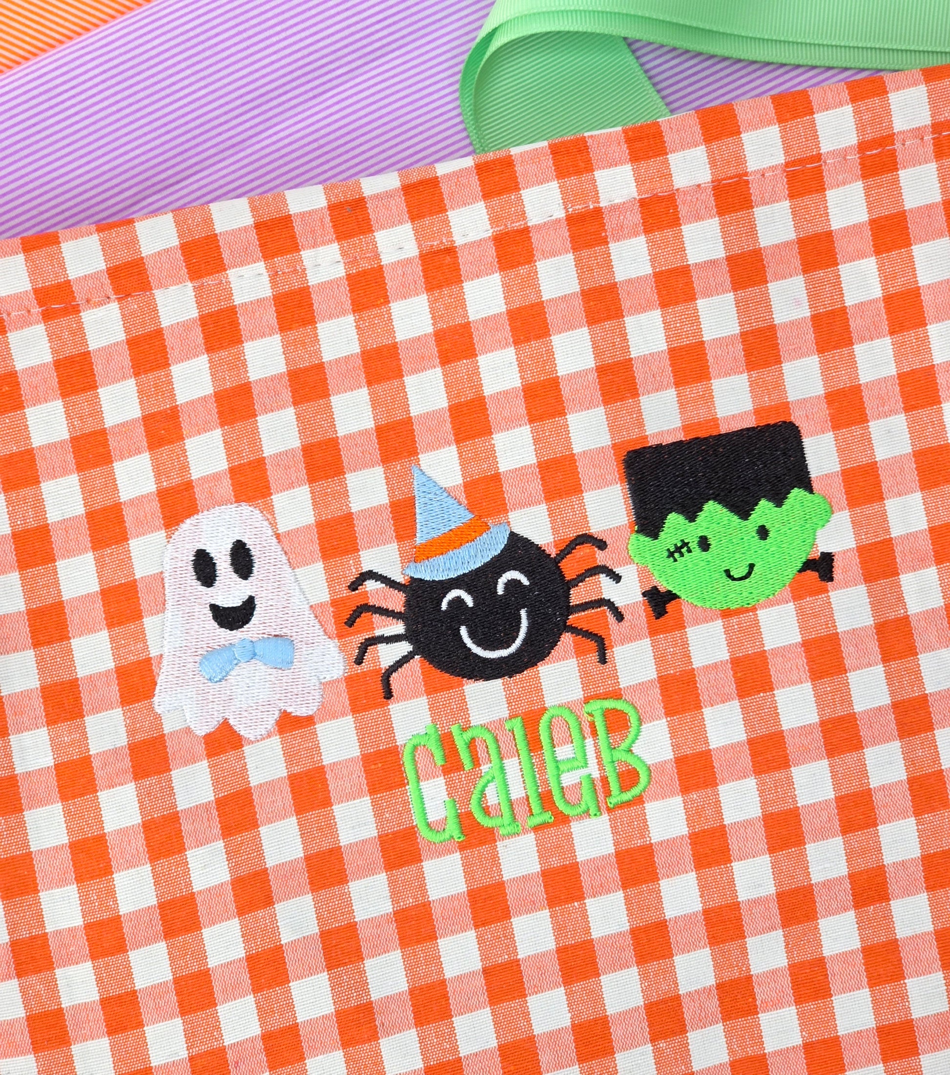 Halloween-themed design with ghost, spider, and green creature on gingham halloween candy basket. Candy pale