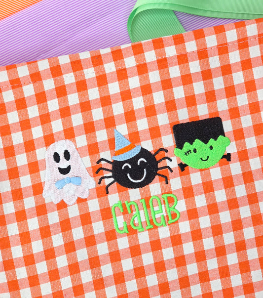 Halloween-themed design with ghost, spider, and green creature on gingham halloween candy basket. Candy pale
