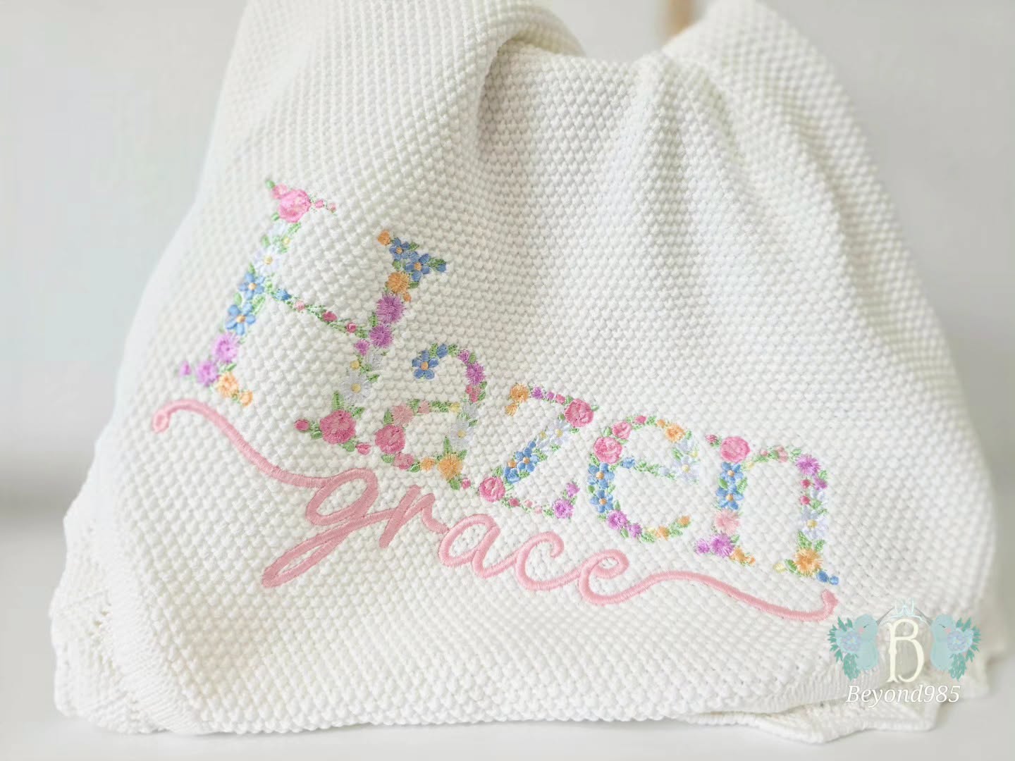 "Personalized ivory knit baby blanket with floral embroidered name and pink script embroidery.
