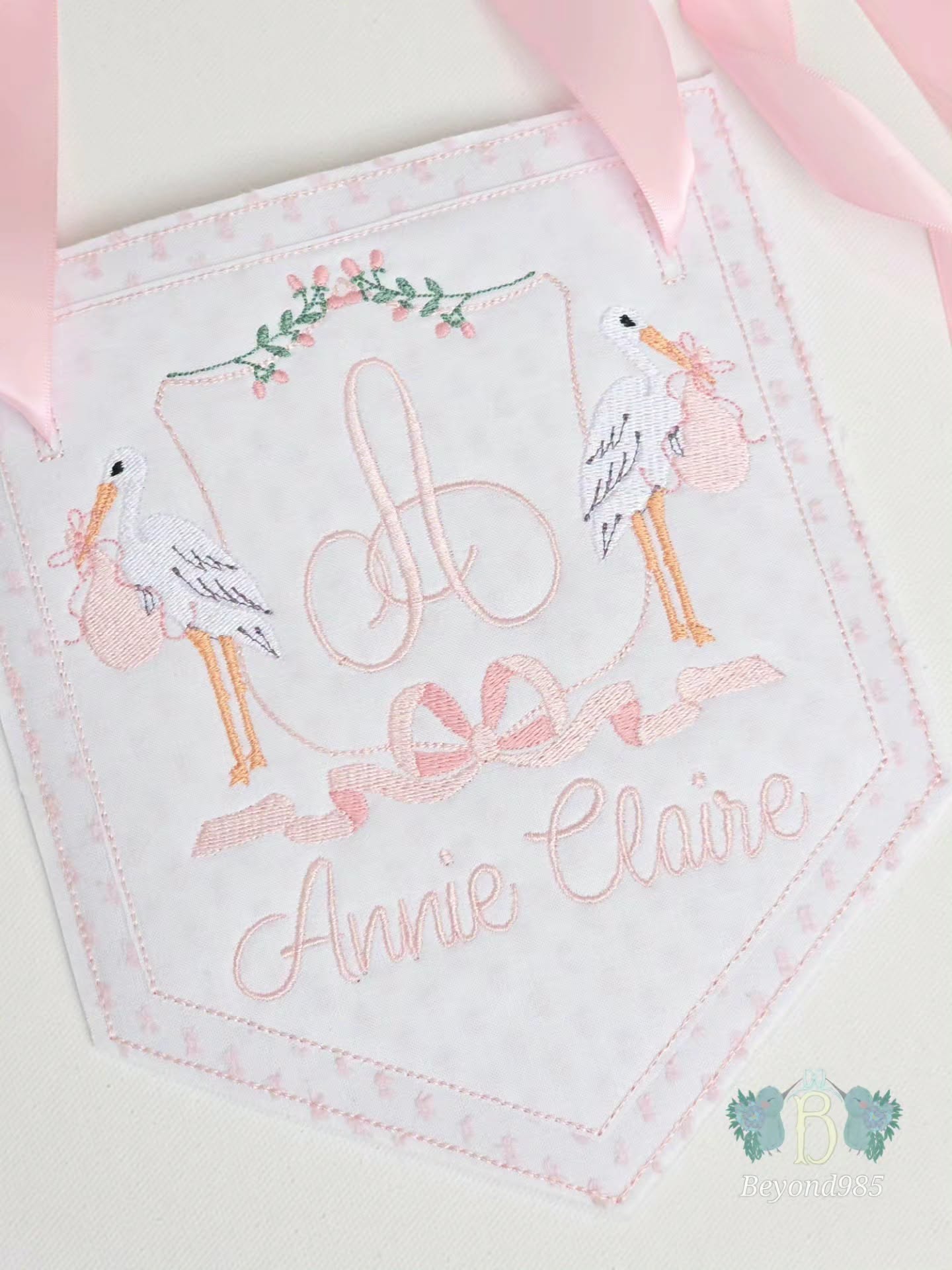 Personalized baby girl door hanger with embroidered monogram, stork design, pink ribbon accents, and custom name embroidery.