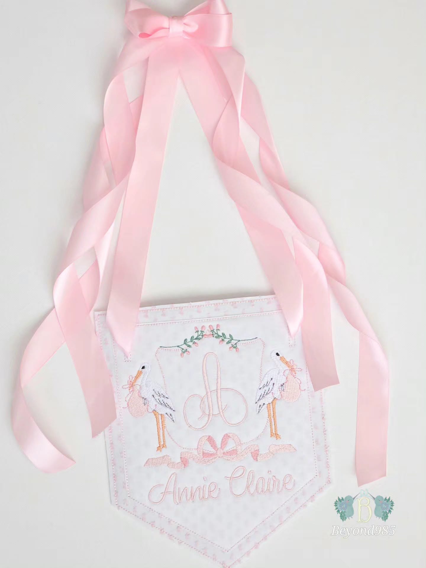 Personalized baby girl door hanger with embroidered monogram, stork design, pink ribbon accents, and custom name embroidery.