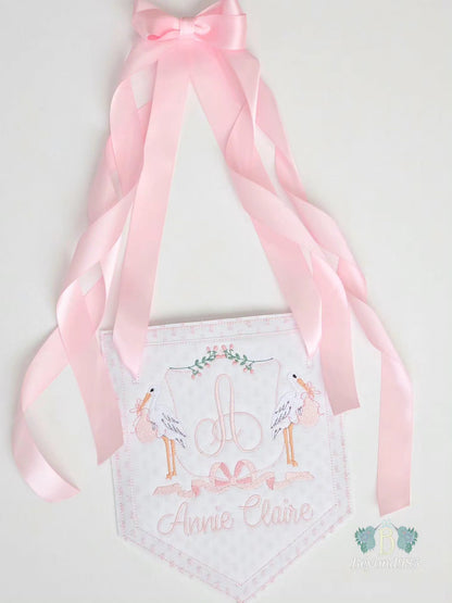Personalized baby girl door hanger with embroidered monogram, stork design, pink ribbon accents, and custom name embroidery.