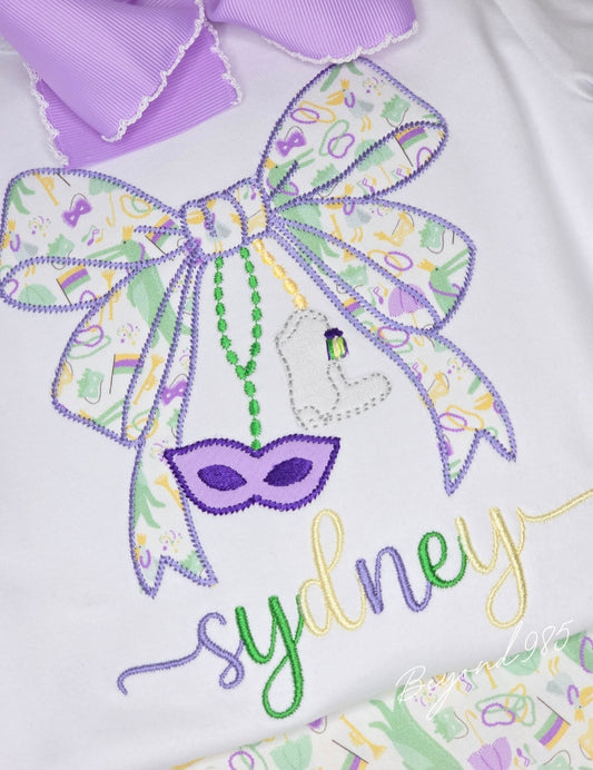 Embroidered design with a bow, mask, and colorful text on a white background