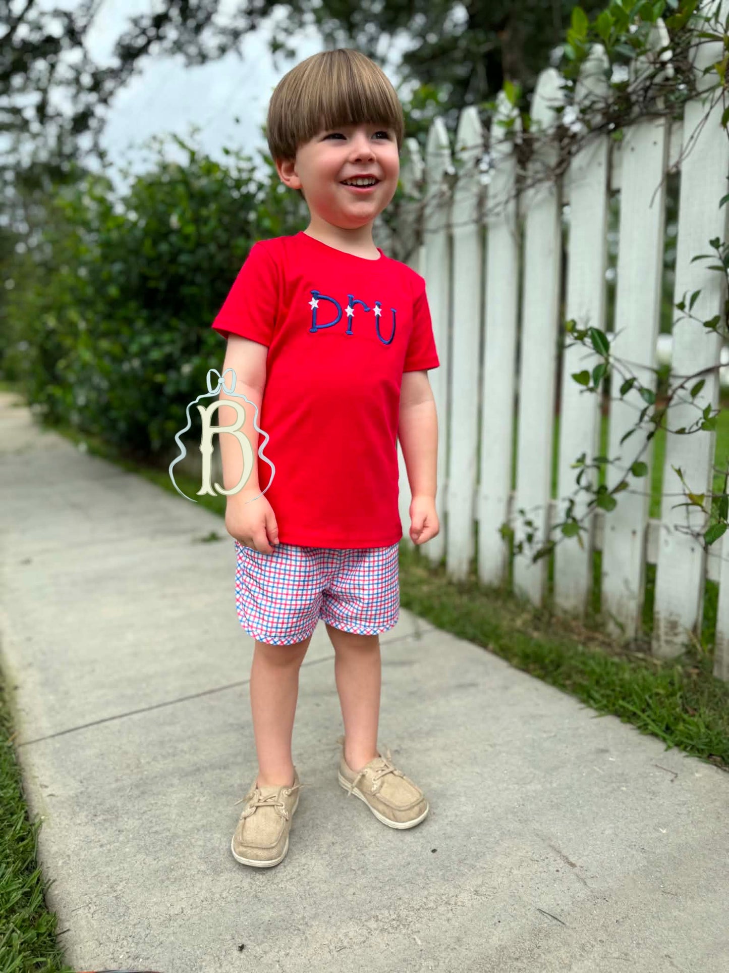Toddler boy wearing personalized red patriotic embroidered shirt with red white and blue plaid shorts
