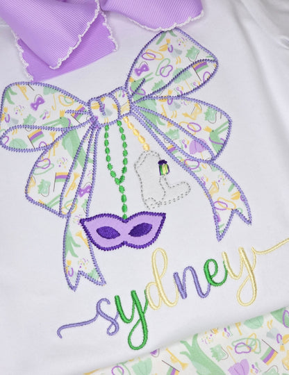 Embroidered design with a bow, mask, and colorful text on a white background