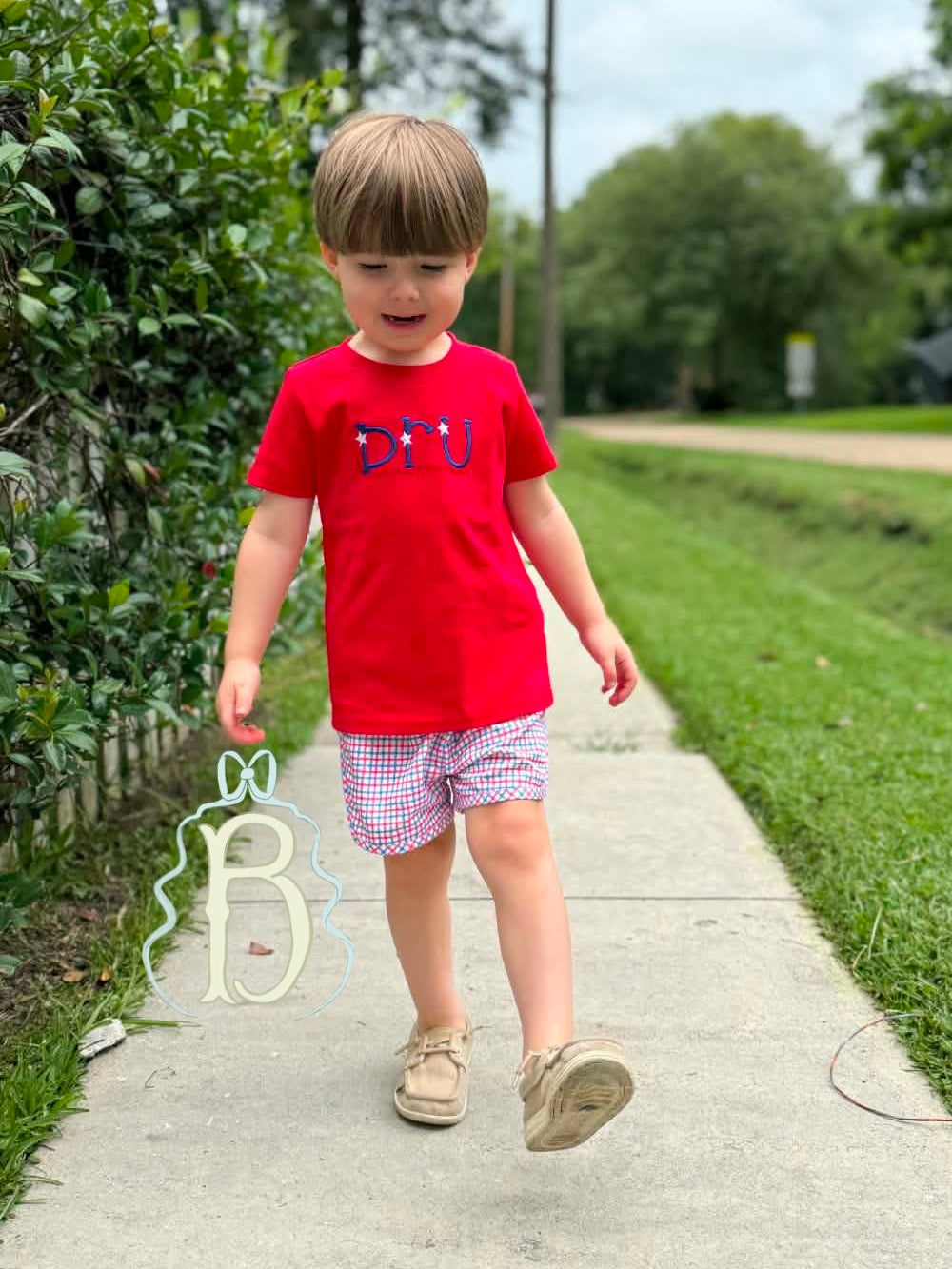 Toddler boy wearing personalized red patriotic embroidered shirt with red white and blue plaid shorts
