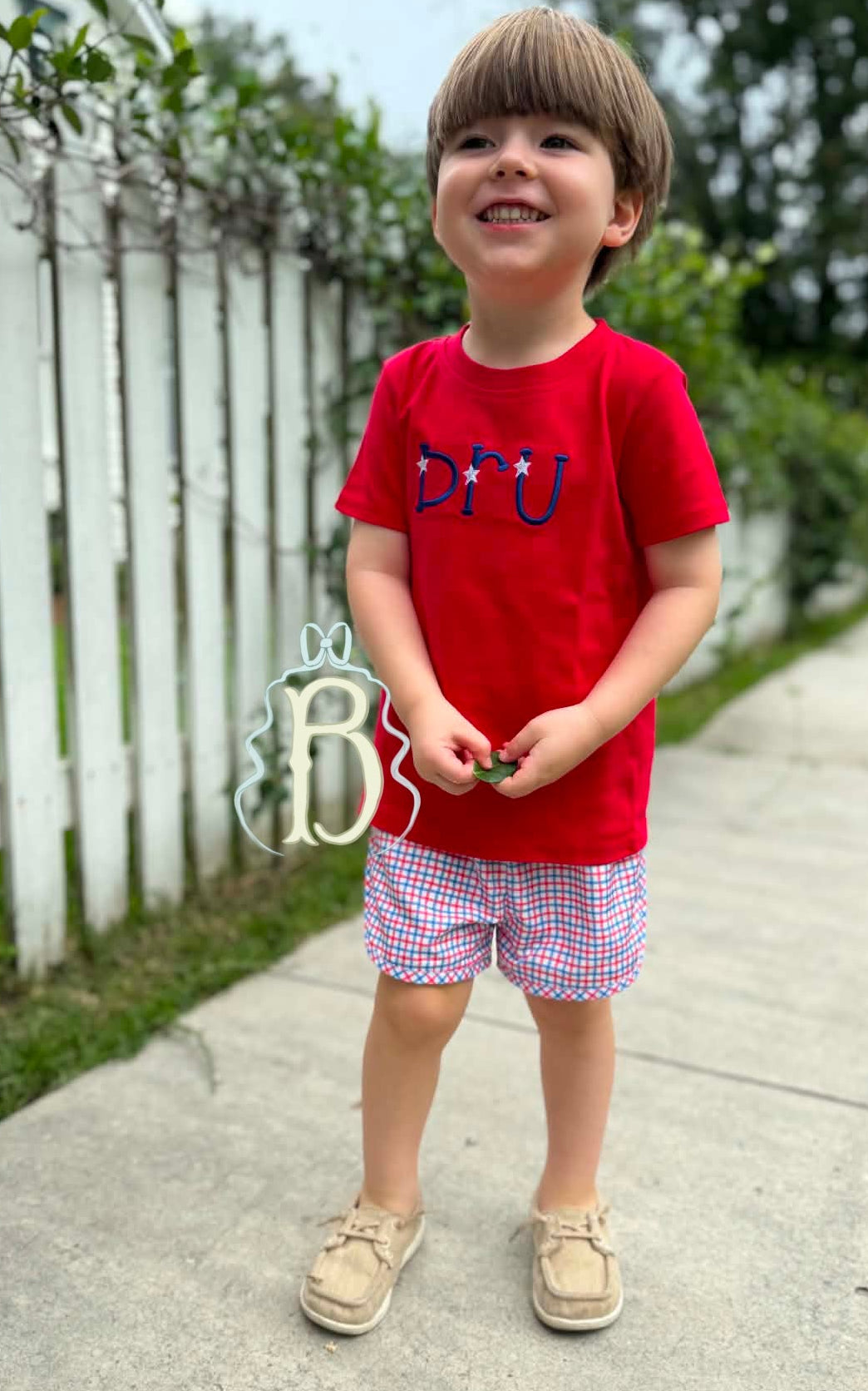 Toddler boy wearing personalized red patriotic embroidered shirt with red white and blue plaid shorts
