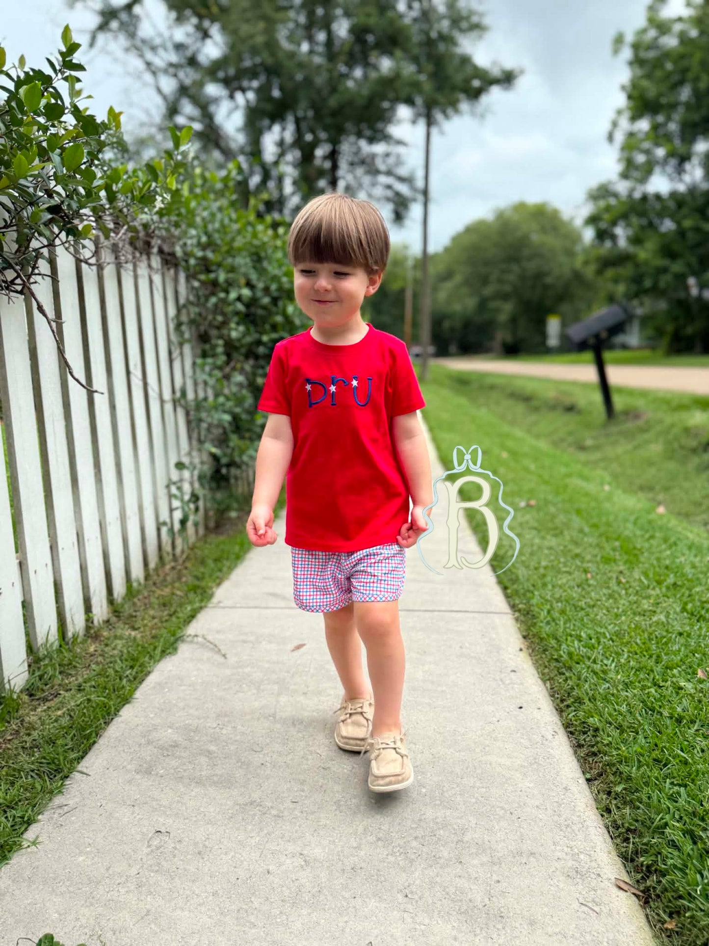 Toddler boy wearing personalized red patriotic embroidered shirt with red white and blue plaid shorts